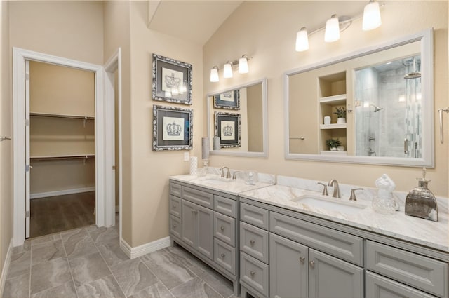 bathroom with double vanity, a spacious closet, a tile shower, and a sink