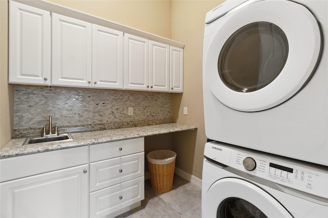 laundry room featuring a sink, cabinet space, stacked washer and clothes dryer, and light tile patterned floors