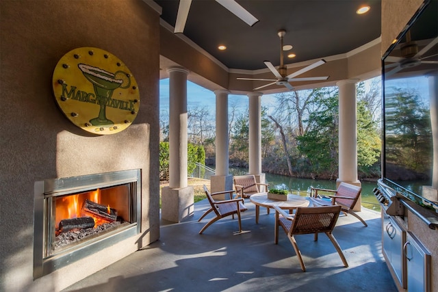 sunroom / solarium featuring ornate columns, a ceiling fan, and a lit fireplace