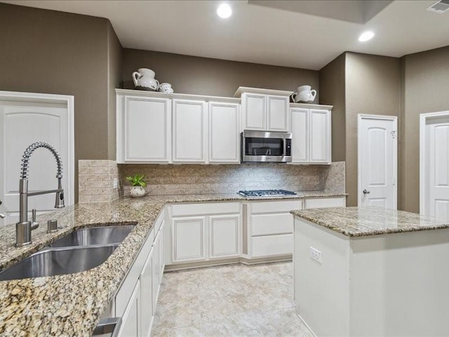 kitchen with sink, white cabinetry, light stone counters, stainless steel appliances, and decorative backsplash