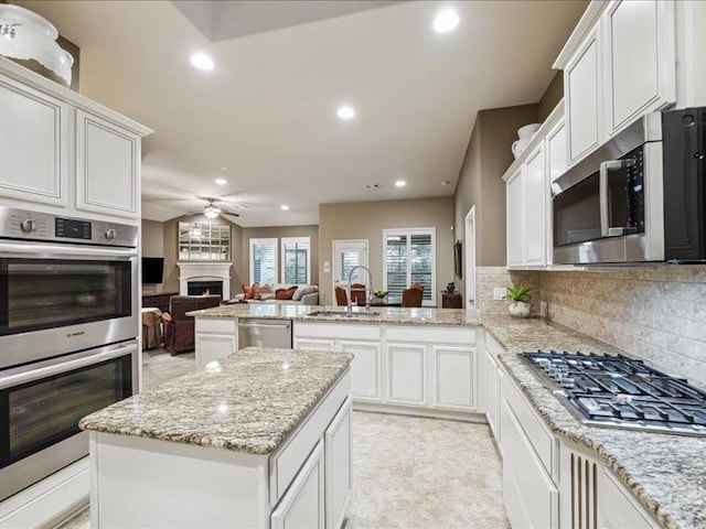 kitchen featuring sink, light stone counters, appliances with stainless steel finishes, kitchen peninsula, and a kitchen island