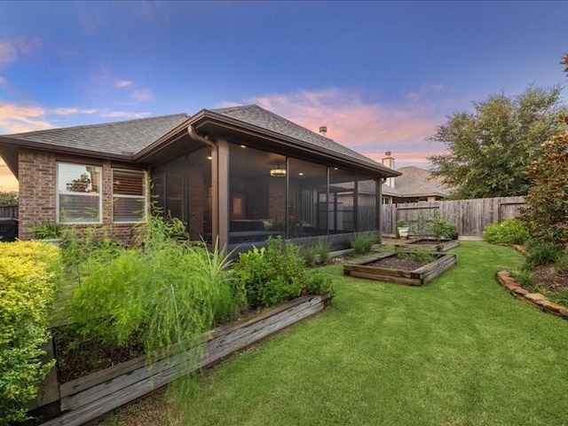 back house at dusk with a sunroom and a lawn