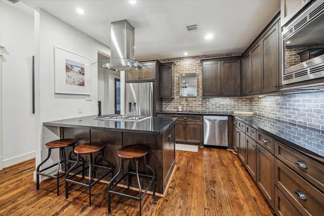 kitchen featuring a breakfast bar, tasteful backsplash, island range hood, dark hardwood / wood-style flooring, and stainless steel appliances