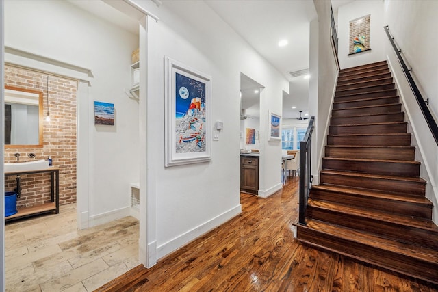 stairs with hardwood / wood-style floors, sink, and brick wall