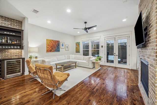 living room with wine cooler, hardwood / wood-style flooring, bar, a brick fireplace, and french doors