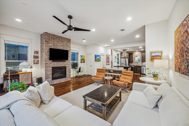 living room featuring hardwood / wood-style floors, a brick fireplace, and ceiling fan