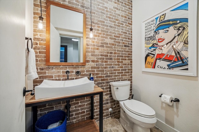 bathroom with brick wall, toilet, and sink