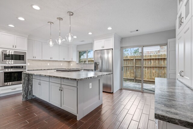 kitchen with pendant lighting, white cabinetry, stainless steel appliances, a center island, and light stone countertops