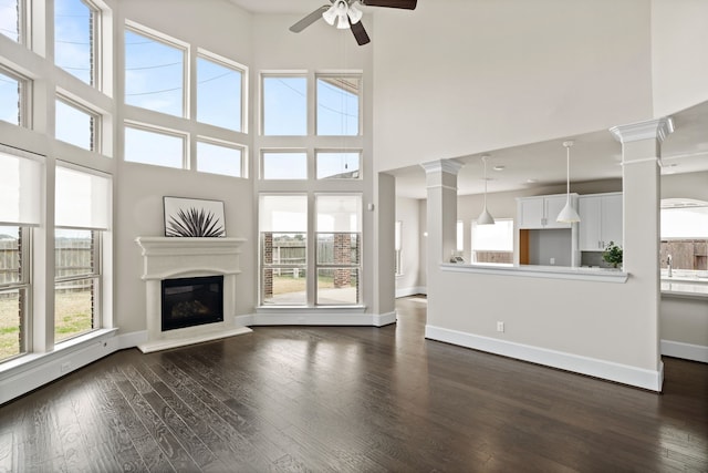 unfurnished living room featuring sink, dark wood-type flooring, decorative columns, and ceiling fan