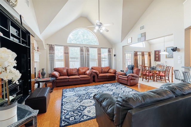 living room with ceiling fan, a high end fireplace, high vaulted ceiling, and wood-type flooring