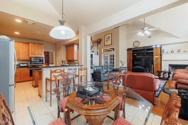 dining room featuring light tile patterned flooring, ceiling fan, a premium fireplace, and high vaulted ceiling