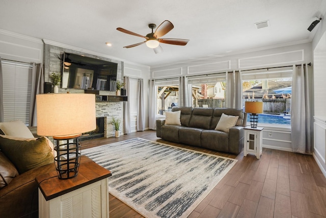 living room with dark wood-type flooring, ceiling fan, ornamental molding, and a fireplace