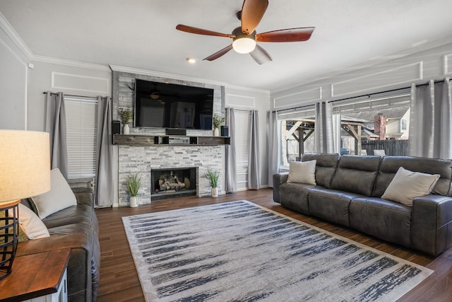 living room featuring ornamental molding, a stone fireplace, ceiling fan, and dark hardwood / wood-style flooring