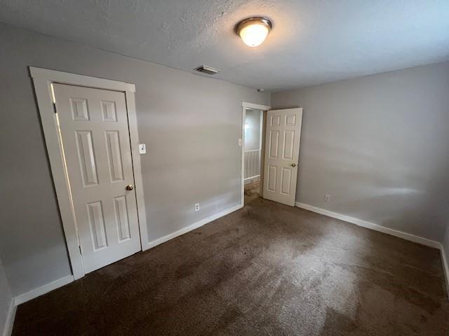 unfurnished bedroom featuring a textured ceiling and dark colored carpet