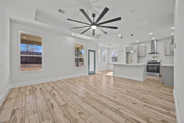 unfurnished living room with a raised ceiling, sink, ceiling fan, and light hardwood / wood-style flooring