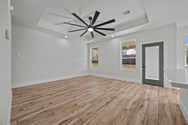 unfurnished room with ceiling fan, a raised ceiling, and light hardwood / wood-style floors