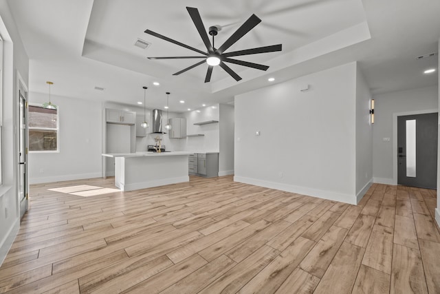 unfurnished living room with a raised ceiling, ceiling fan, and light hardwood / wood-style floors