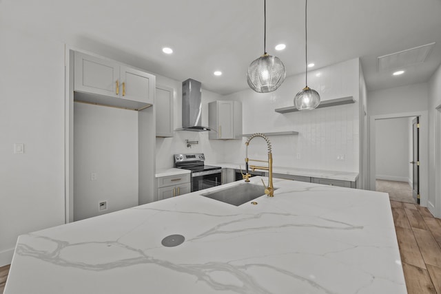 kitchen featuring electric stove, wall chimney range hood, pendant lighting, sink, and light stone counters