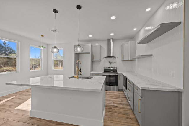 kitchen with electric stove, wall chimney range hood, sink, and an island with sink