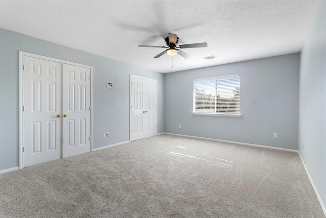 unfurnished bedroom featuring ceiling fan, two closets, light colored carpet, and a textured ceiling