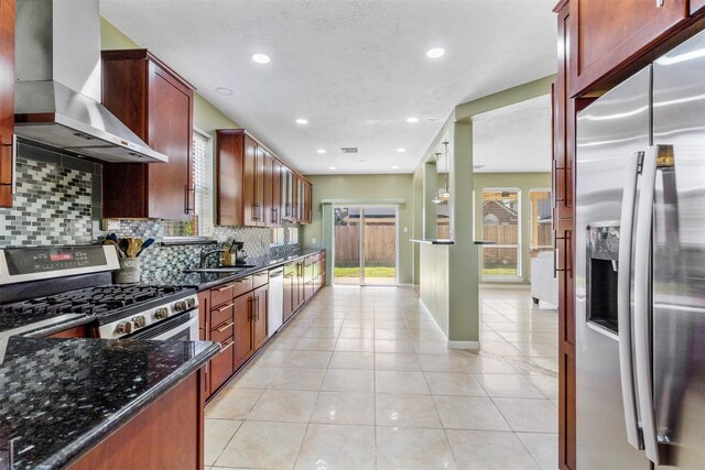 kitchen featuring light tile patterned flooring, tasteful backsplash, dark stone counters, stainless steel appliances, and wall chimney range hood