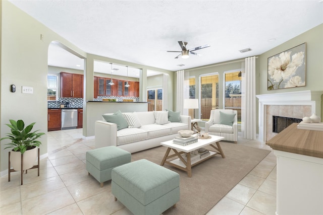 living room featuring light tile patterned floors, a textured ceiling, a tile fireplace, and ceiling fan