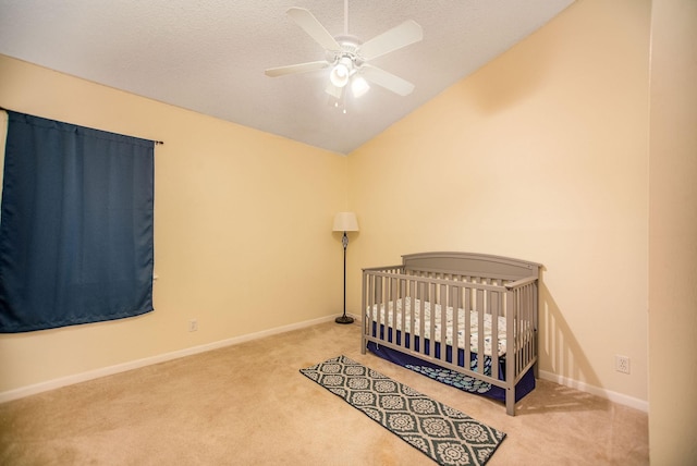 carpeted bedroom featuring vaulted ceiling, a nursery area, ceiling fan, and a textured ceiling