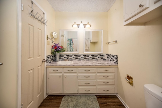 bathroom featuring backsplash, hardwood / wood-style floors, vanity, a textured ceiling, and toilet