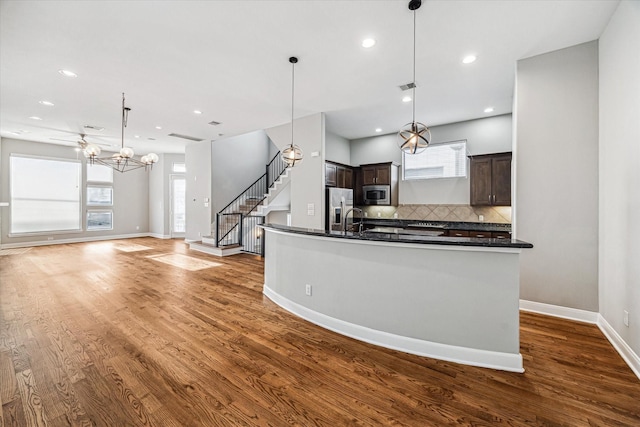 kitchen with stainless steel appliances, decorative light fixtures, dark brown cabinets, and a center island with sink