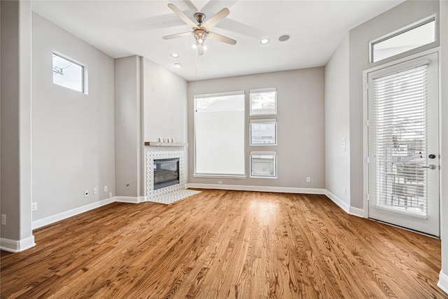 unfurnished living room with plenty of natural light, a tile fireplace, ceiling fan, and light wood-type flooring