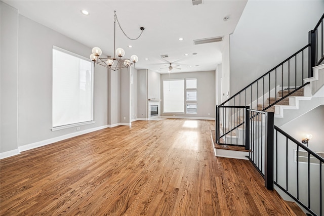 unfurnished living room with ceiling fan with notable chandelier and hardwood / wood-style floors