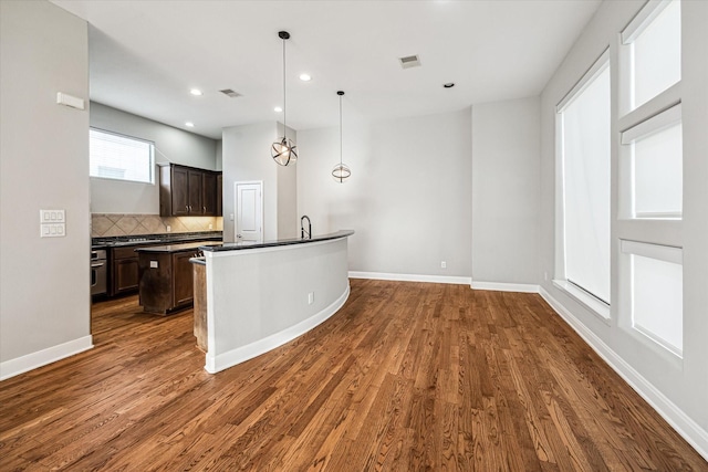 kitchen with pendant lighting, an island with sink, dark hardwood / wood-style flooring, decorative backsplash, and dark brown cabinetry