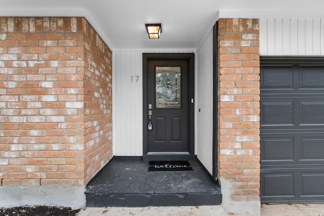 view of exterior entry with a garage and brick siding