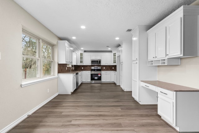 kitchen featuring visible vents, glass insert cabinets, stainless steel appliances, white cabinetry, and built in desk