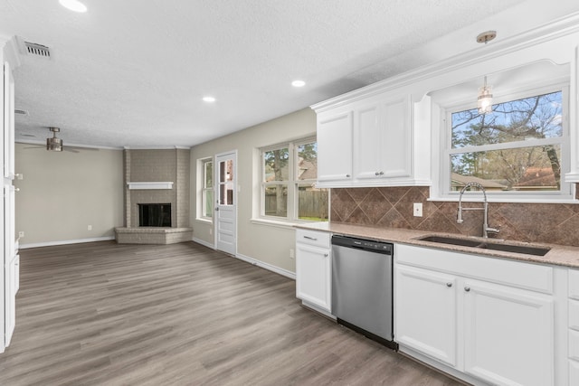 kitchen featuring a sink, visible vents, white cabinetry, a brick fireplace, and dishwasher