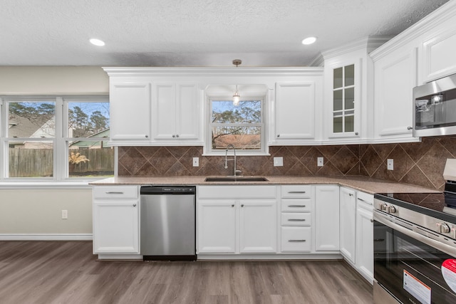 kitchen featuring stainless steel appliances, a sink, light wood-style floors, white cabinets, and glass insert cabinets