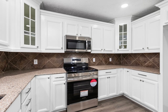 kitchen featuring stainless steel appliances, white cabinets, glass insert cabinets, and light stone countertops