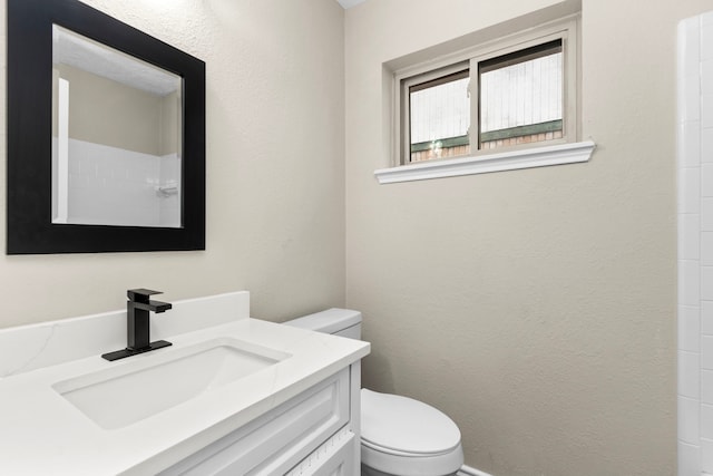 full bath featuring toilet, a textured wall, and vanity