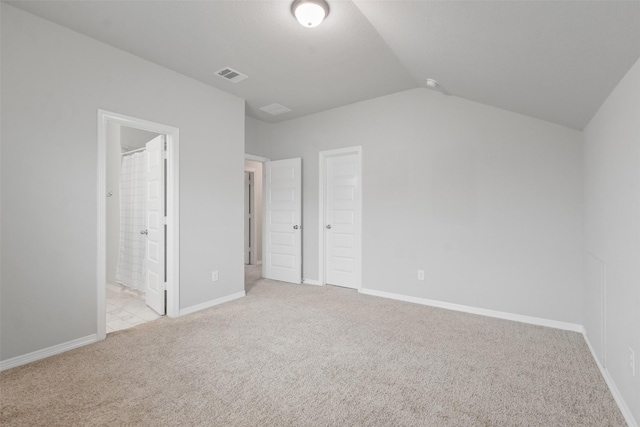 unfurnished bedroom featuring light colored carpet, lofted ceiling, and ensuite bathroom