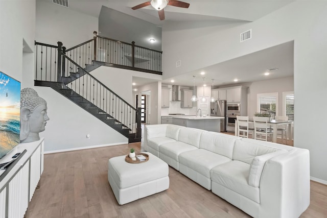 living room with a high ceiling, sink, ceiling fan, and light hardwood / wood-style flooring