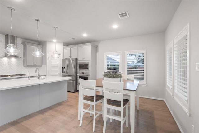 kitchen featuring appliances with stainless steel finishes, sink, decorative backsplash, hanging light fixtures, and wall chimney exhaust hood