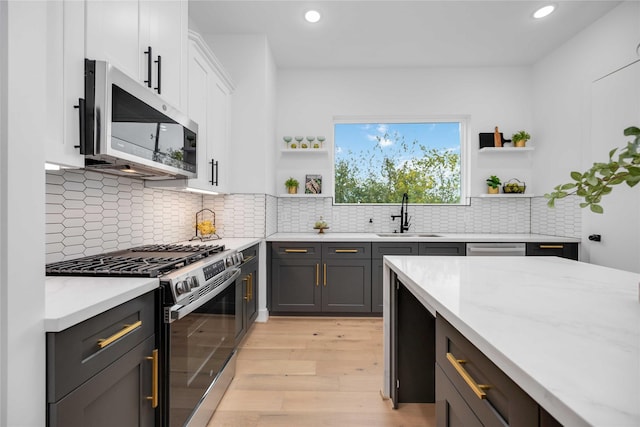 kitchen with sink, light hardwood / wood-style flooring, appliances with stainless steel finishes, white cabinetry, and light stone counters