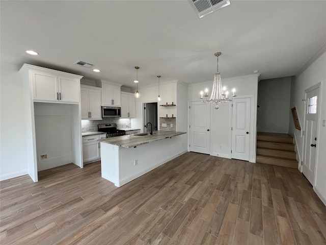 kitchen featuring hanging light fixtures, light wood-type flooring, appliances with stainless steel finishes, dark stone counters, and white cabinets