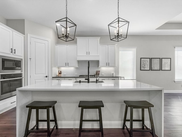 kitchen with black microwave, oven, white cabinets, and a center island with sink