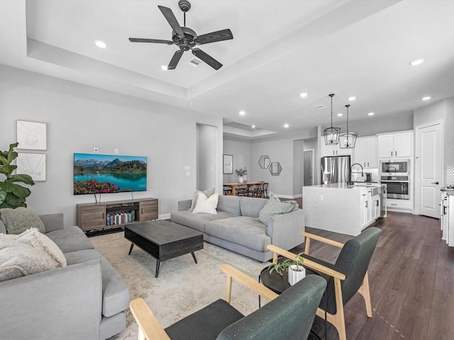 living room featuring a raised ceiling, ceiling fan, sink, and dark hardwood / wood-style flooring