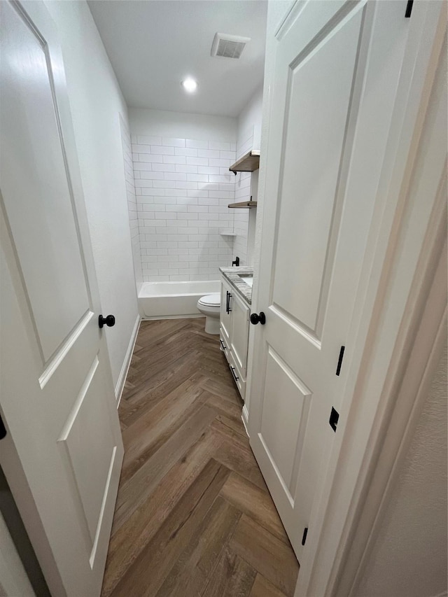 full bathroom featuring vanity, parquet floors, tiled shower / bath combo, and toilet