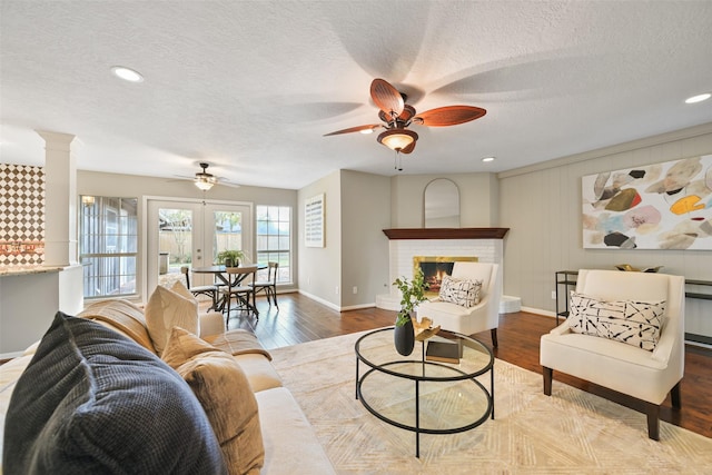 living room featuring ornate columns, a textured ceiling, hardwood / wood-style flooring, ceiling fan, and a fireplace