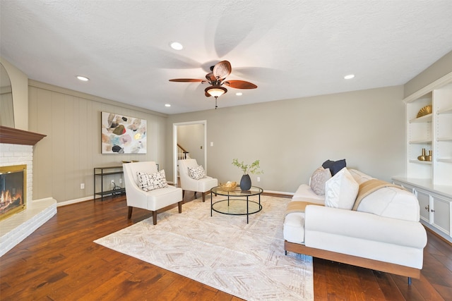 living room featuring a brick fireplace, hardwood / wood-style flooring, a textured ceiling, and ceiling fan