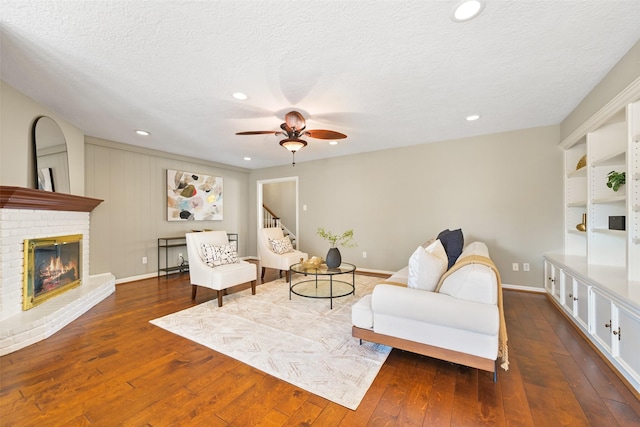 living room with ceiling fan, a textured ceiling, a fireplace, and dark hardwood / wood-style flooring