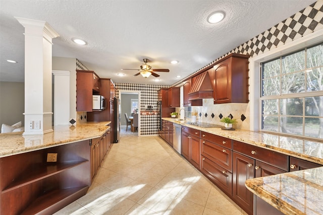 kitchen with light stone counters, stainless steel appliances, decorative columns, and premium range hood